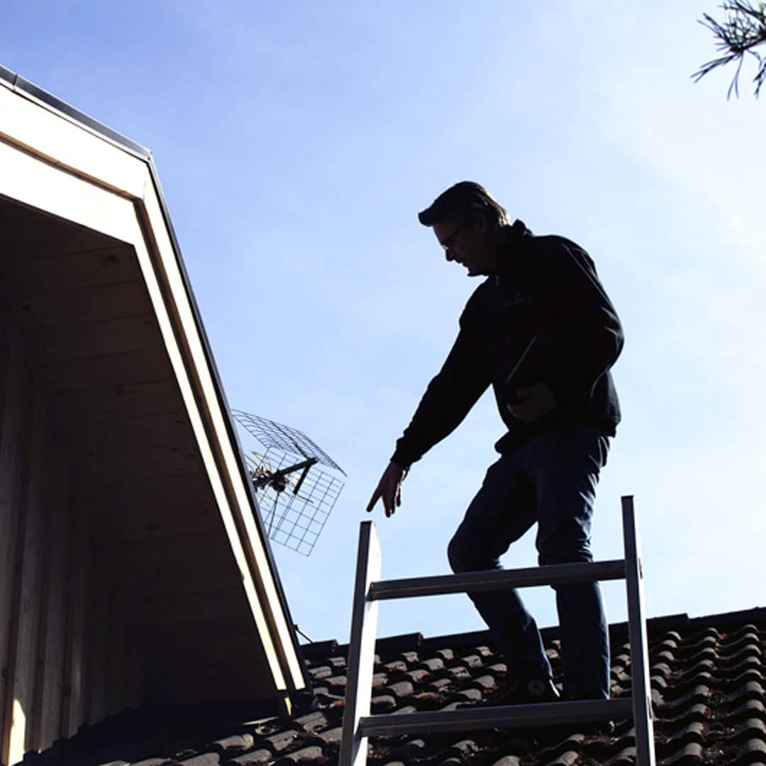 Besiktningsman besiktigar tak på ett hus och pekar på fel