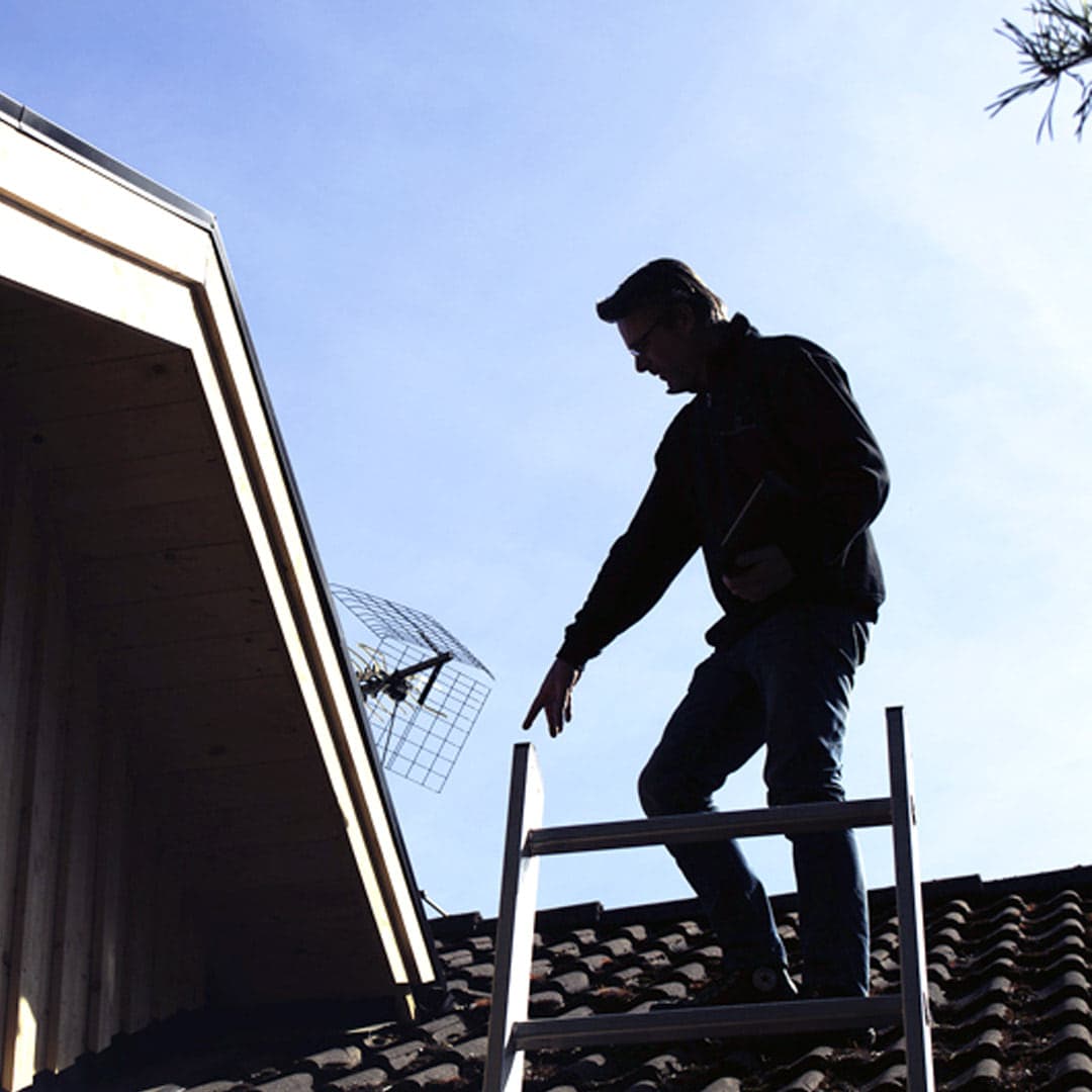 Besiktningsman besiktigar tak på ett hus och pekar på fel